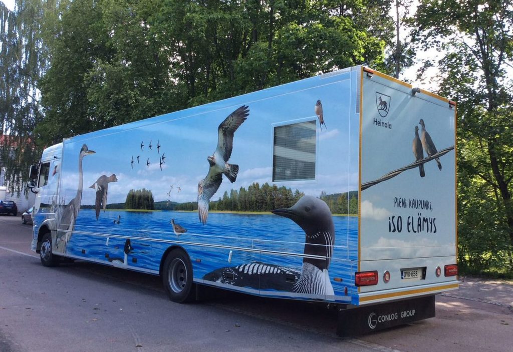 Kirjastoauto Sulka, jonka kyljessä lintujen kuvia järvimaisemassa..