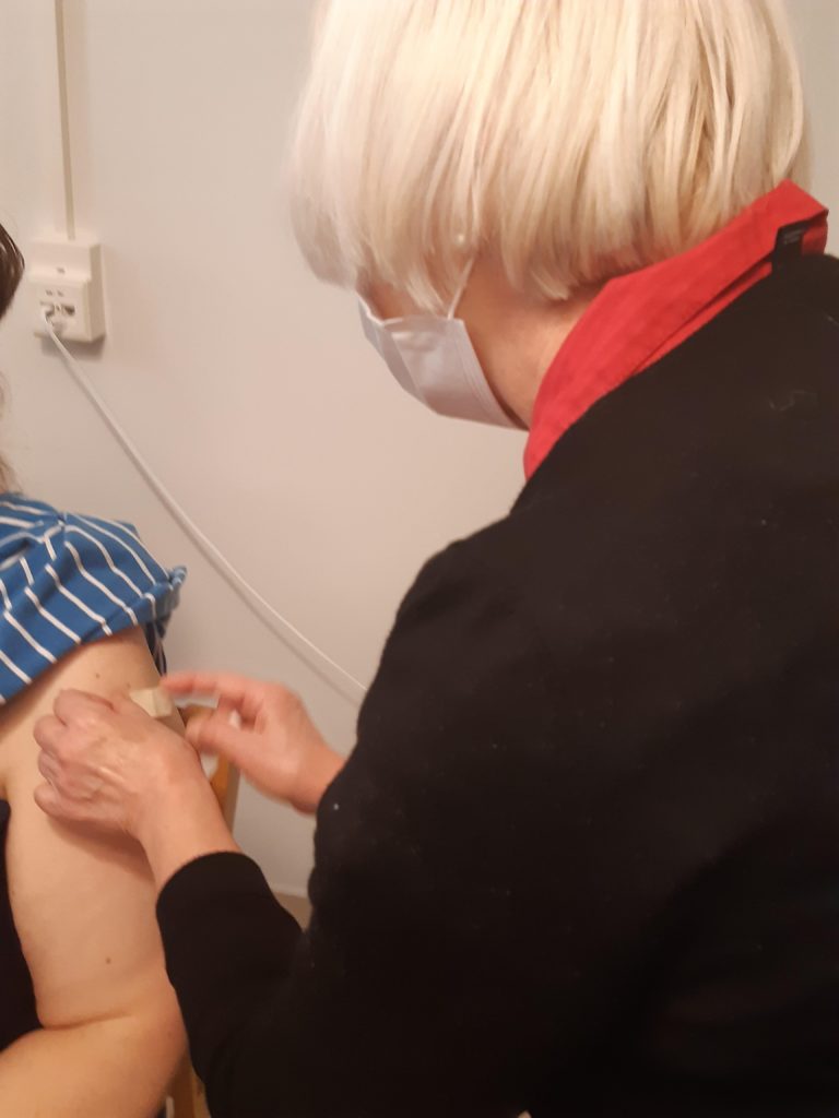 Terveydenhoitaja kiinnittää laastarin olkavarteen.