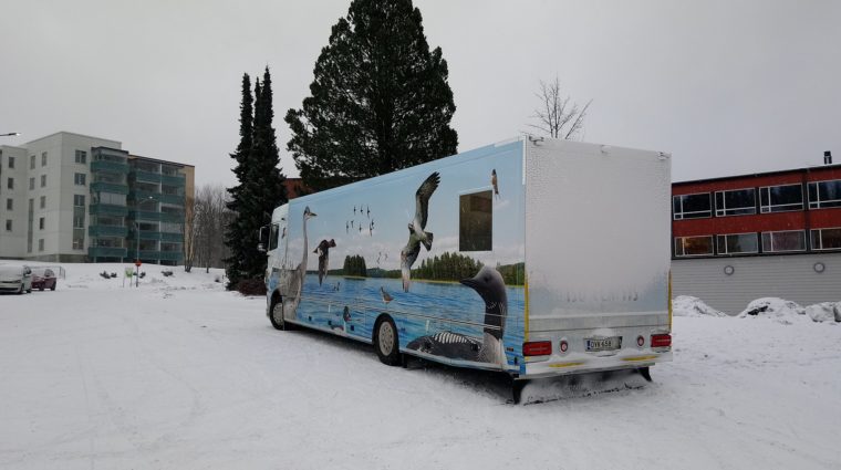 Kirjastoauto Sulka talvisessa kaupunkimaisemassa takaa sivulta kuvattuna.