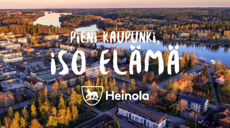 Kuva Heinolan keskustasta auringonlaskun aikaan. Kuvassa iso logo.