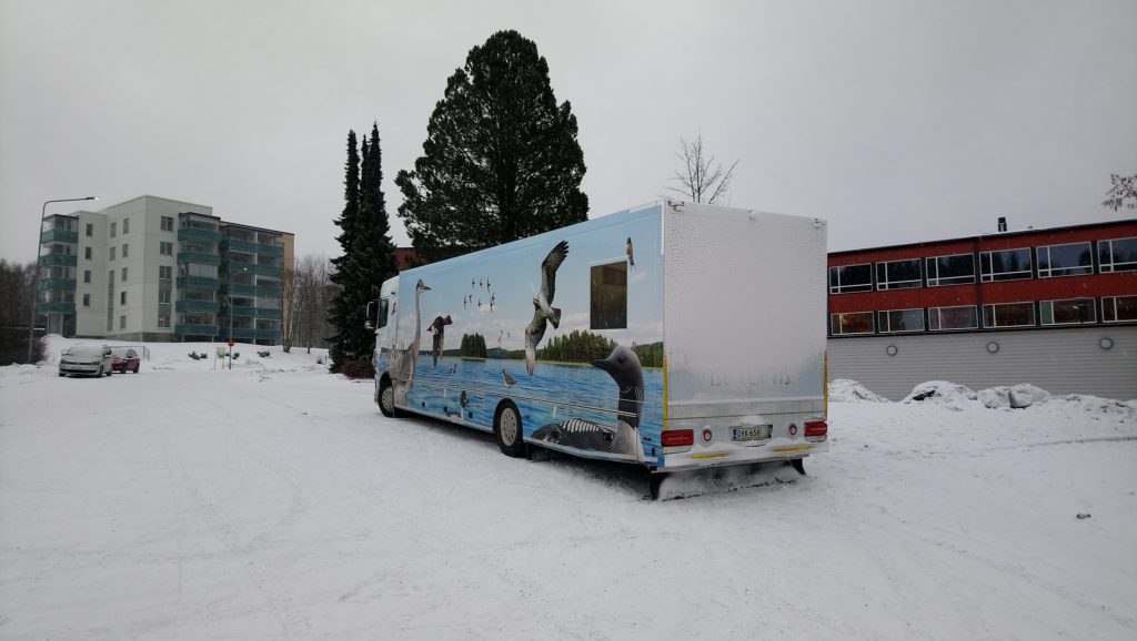 Kirjastoauto talvipäivänä lumisessa kaupunkimaisemassa