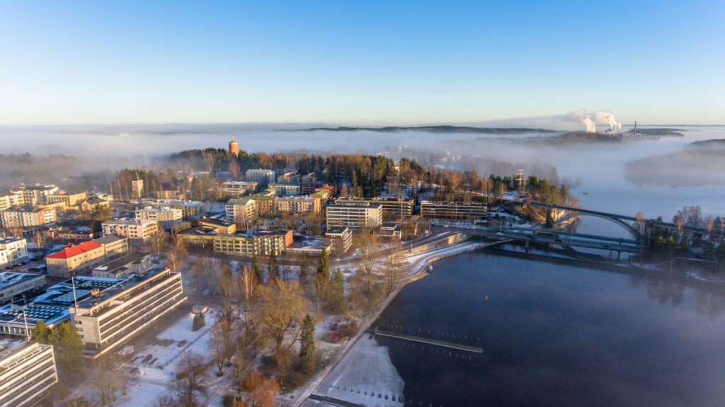 Rantapuisto ja kaupunkia ilmasta kuvattuna: vettä, puita ja rakennuksia.