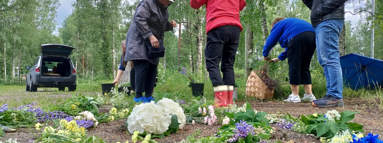 Asukkkaat rakentavat kukkaspriraalia vesisateessa Mustikkahaan hiekkakentällä