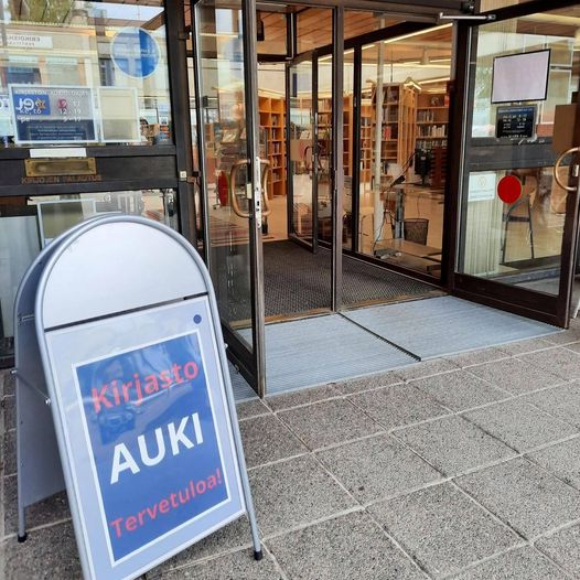 Kirjaston ulko-ovet auki, standissa teksti kirjasto on auki.