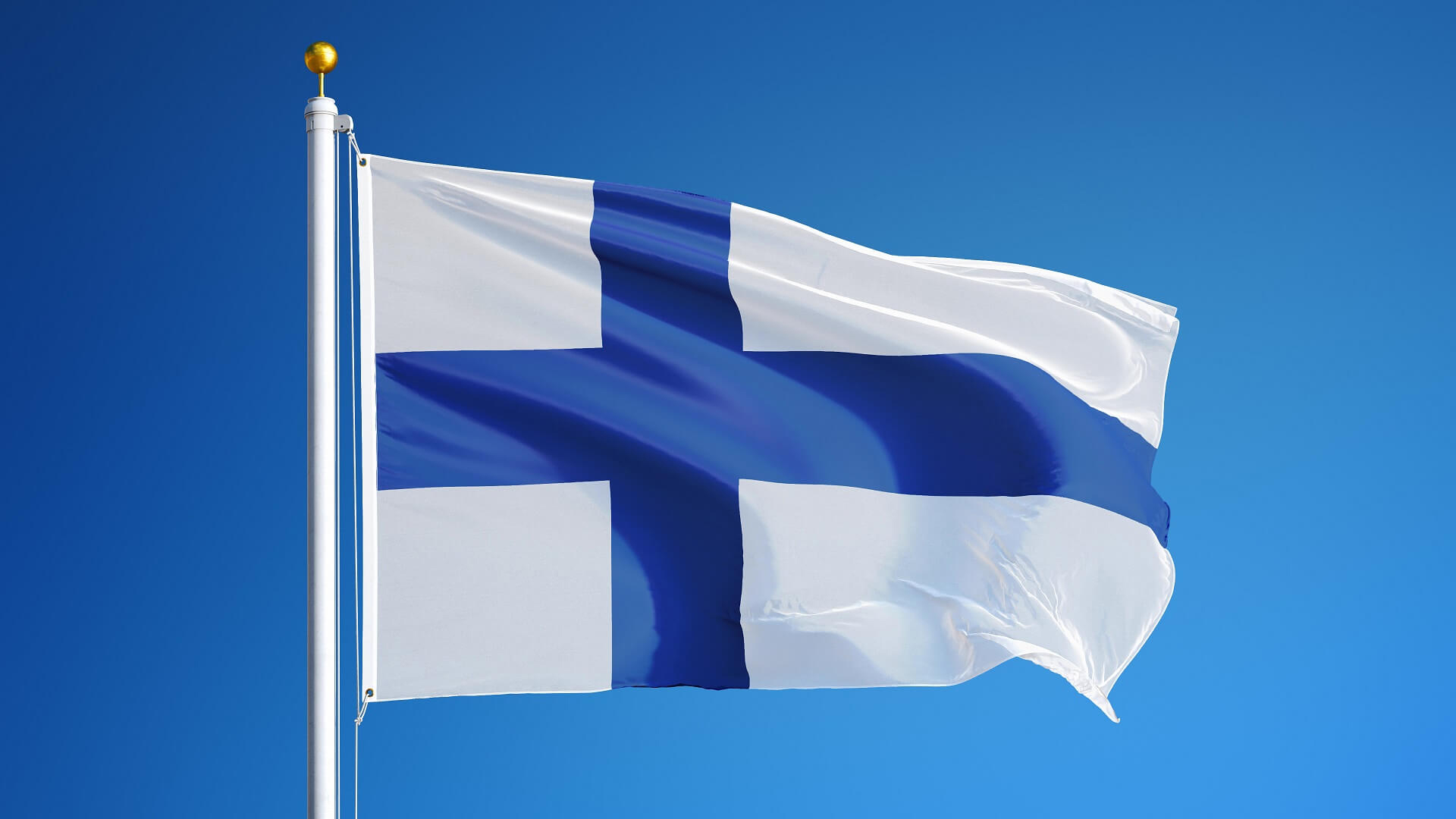 Suomen lippu lipputangossa sinistä taivasta vasten.