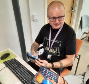 Kahdella henkilöillä pöydän ääressä älypuhelimia kädessä, tietokoneen näppäimistö pöydällä.