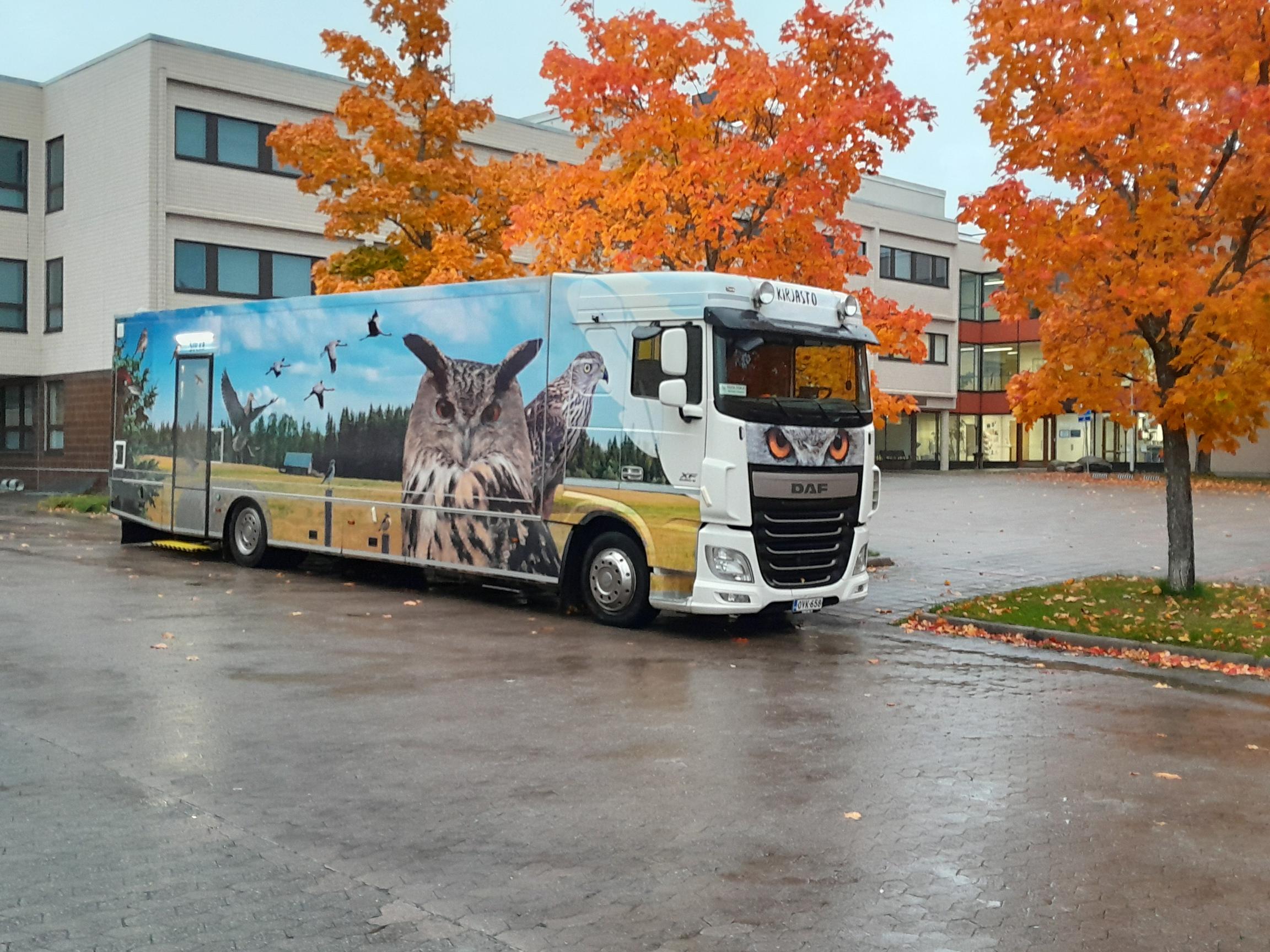 Kirjastoauto kaupungintalon edessä, puissa ruskaa.