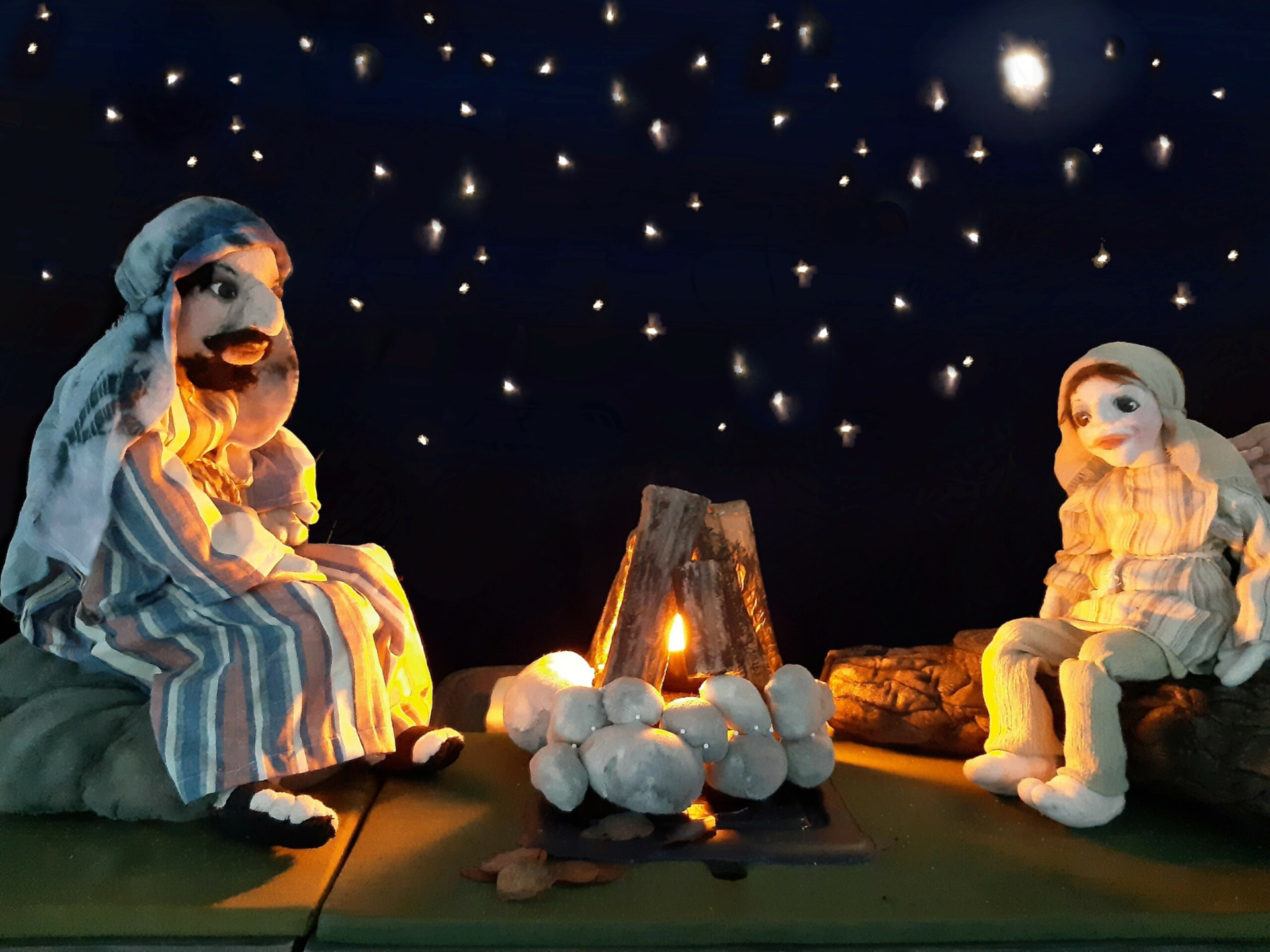 Kaksi paimen-nukkea istuu nuotiolla tähtitaivaan alla.