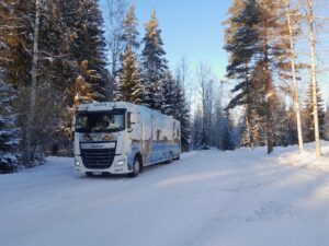 Heinolan kirjastoauto Sulka talvimaisemassa tiellä puiden alla.