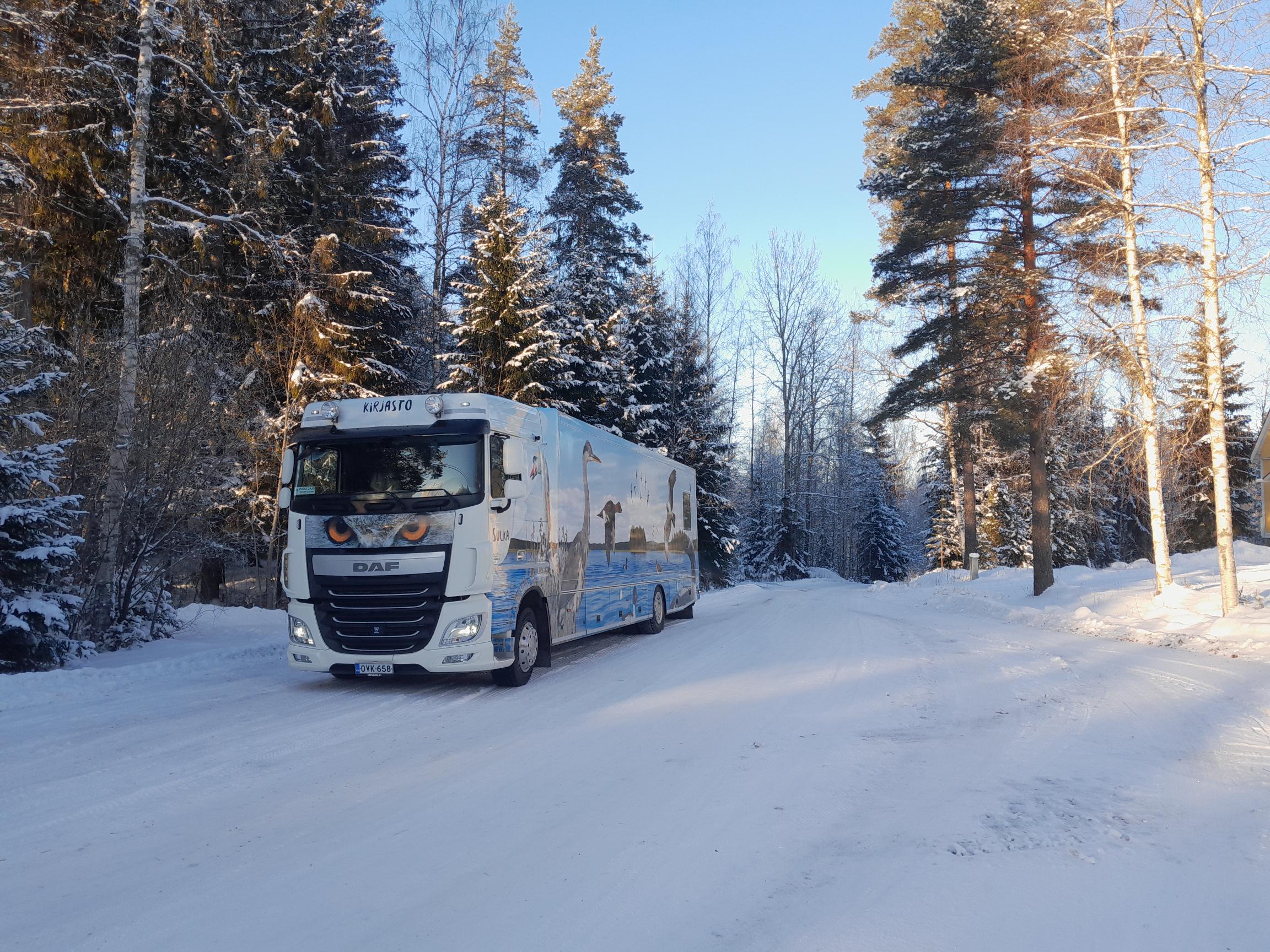 Heinolan kirjastoauto Sulka talvimaisemassa tiellä puiden alla.