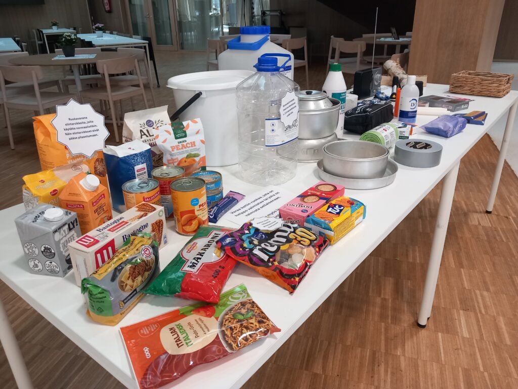 Kuvassa kodin kotivaran esimerkkejä mm. elintarvikkeita, ensiapu- ja hygieniavälineitä sekä vesiastioita. 