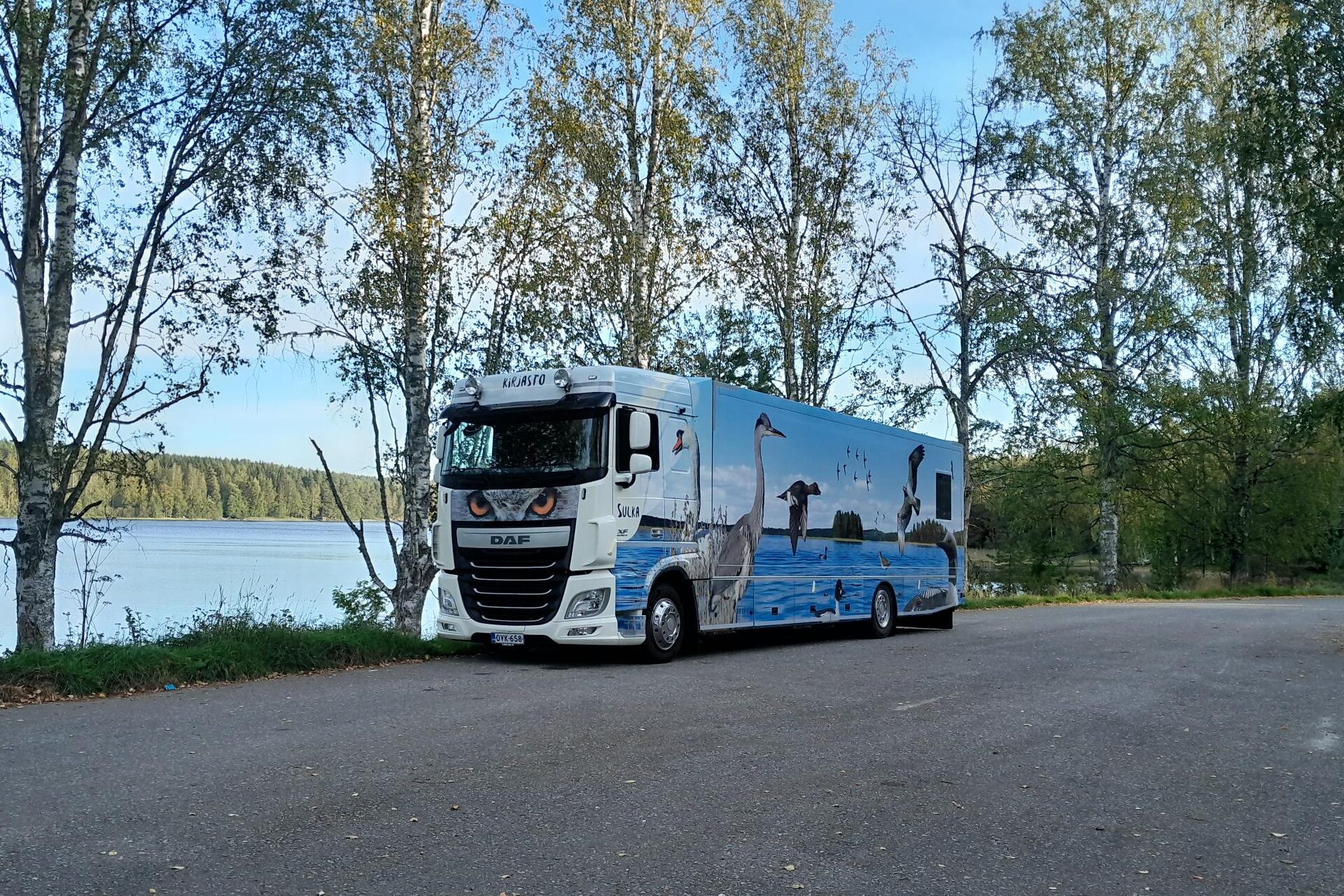 Kirjastoauto Sulka kesämaisemassa rantatiellä koivujen alla.