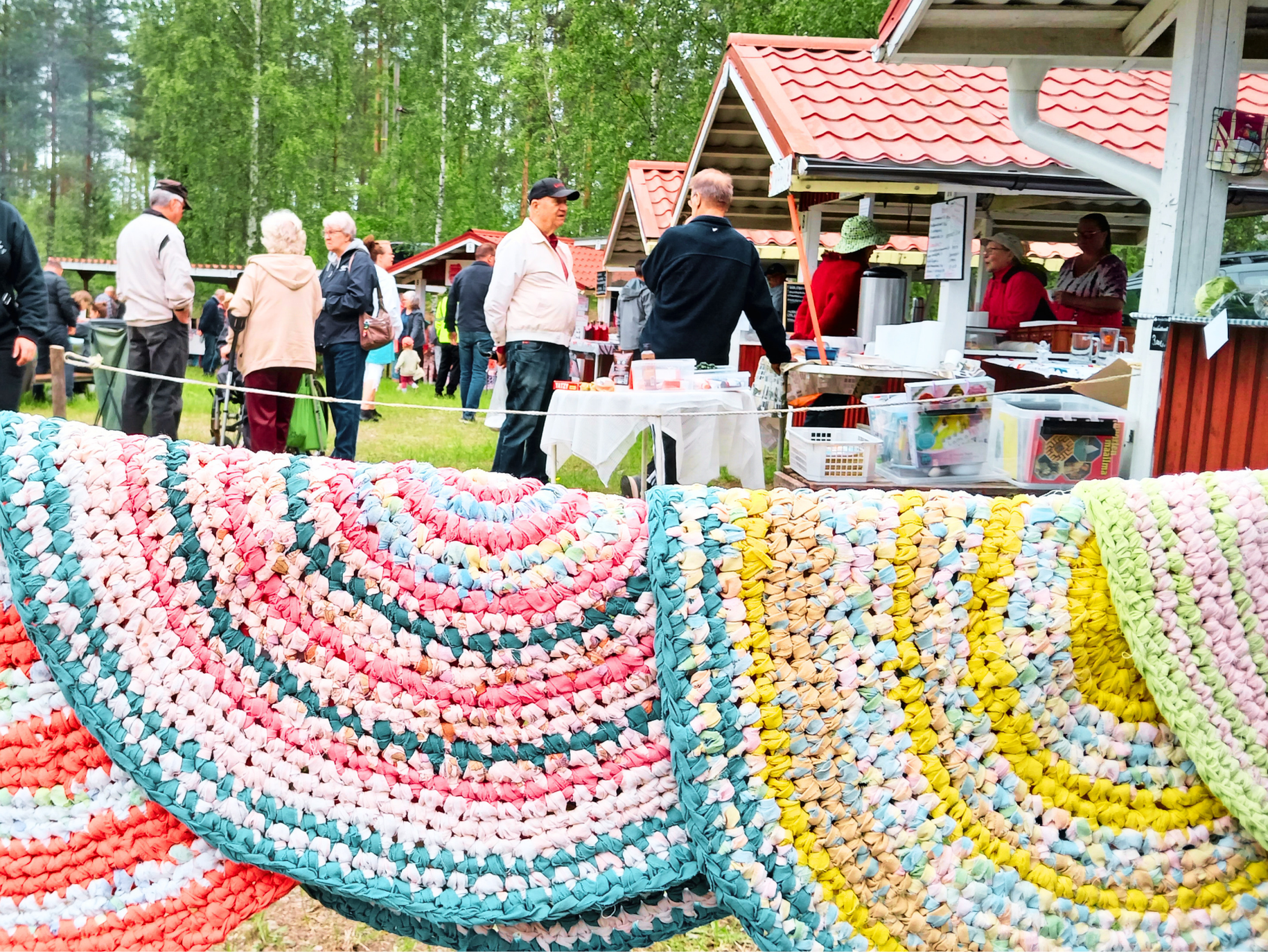 Värikkäitä  vikrattuja mattoja naurlla, taustalla ihmisiä markkinoilla.