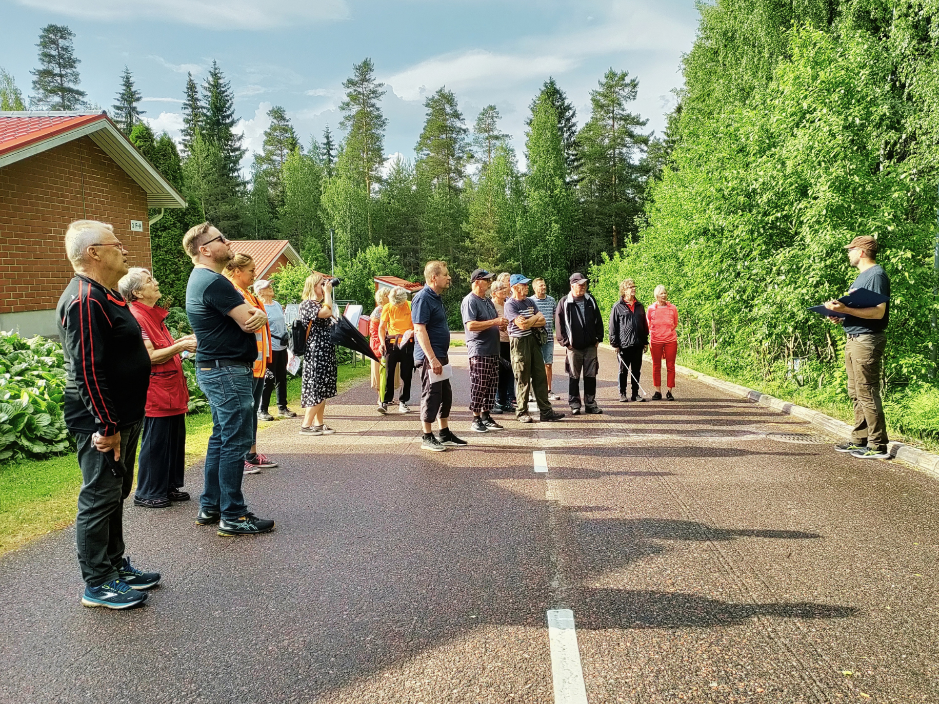 Ihmisiä seisoo kadulla, taustalla puita.